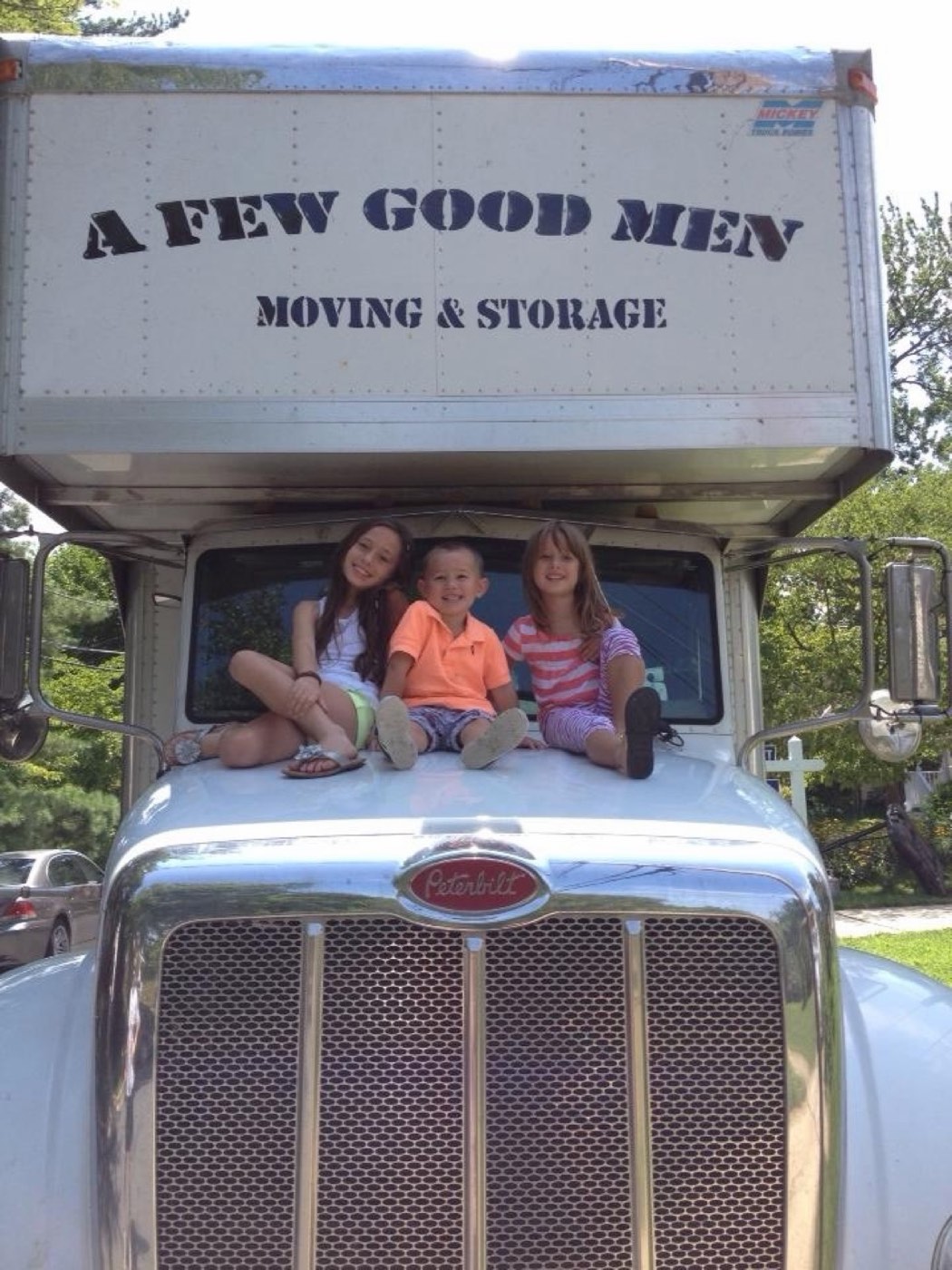 Three kids sitting on the hood of an A Few Good Men moving truck