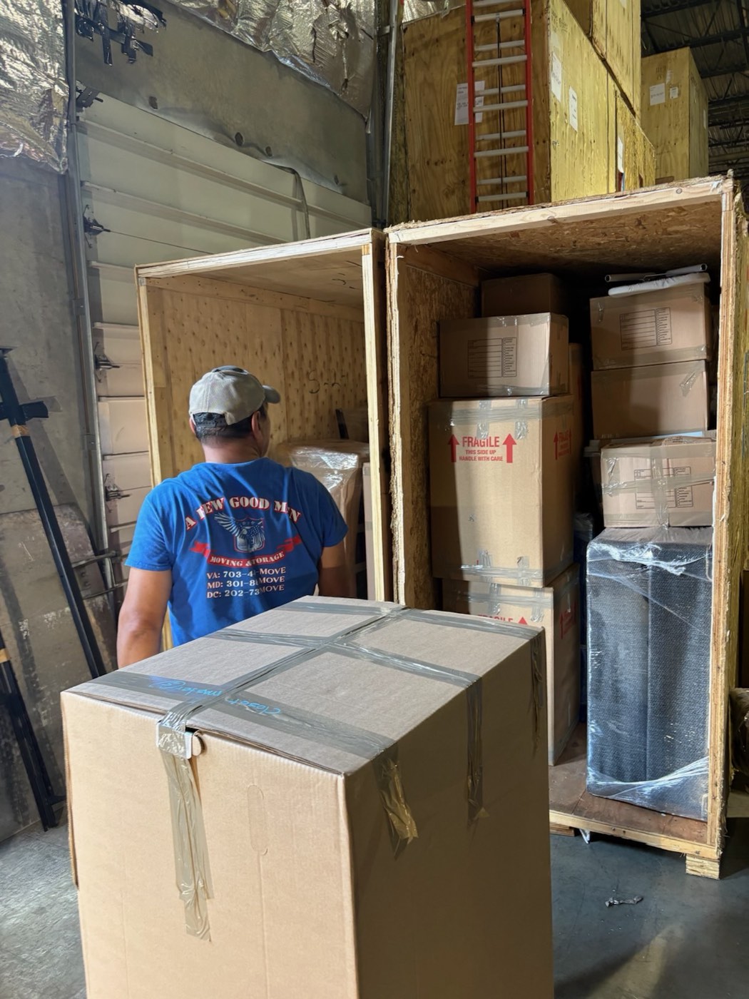 A mover loading boxes into a wooden storage vault at the A Few Good Men warehouse