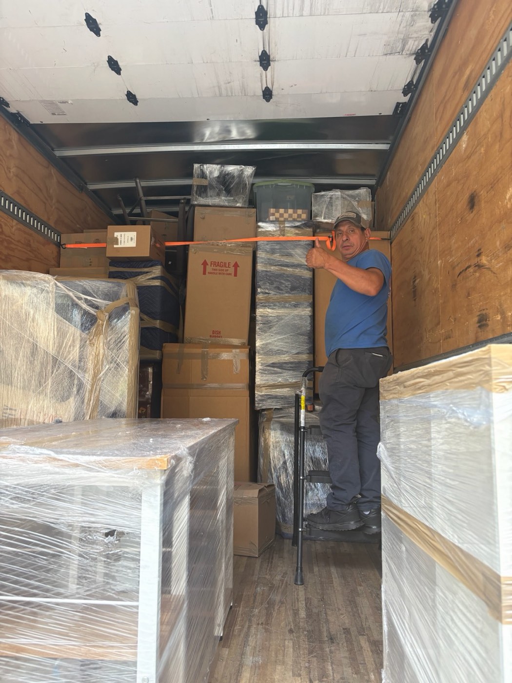 A mover securing a load of shrink-wrapped furniture and boxes inside an A Few Good Men truck