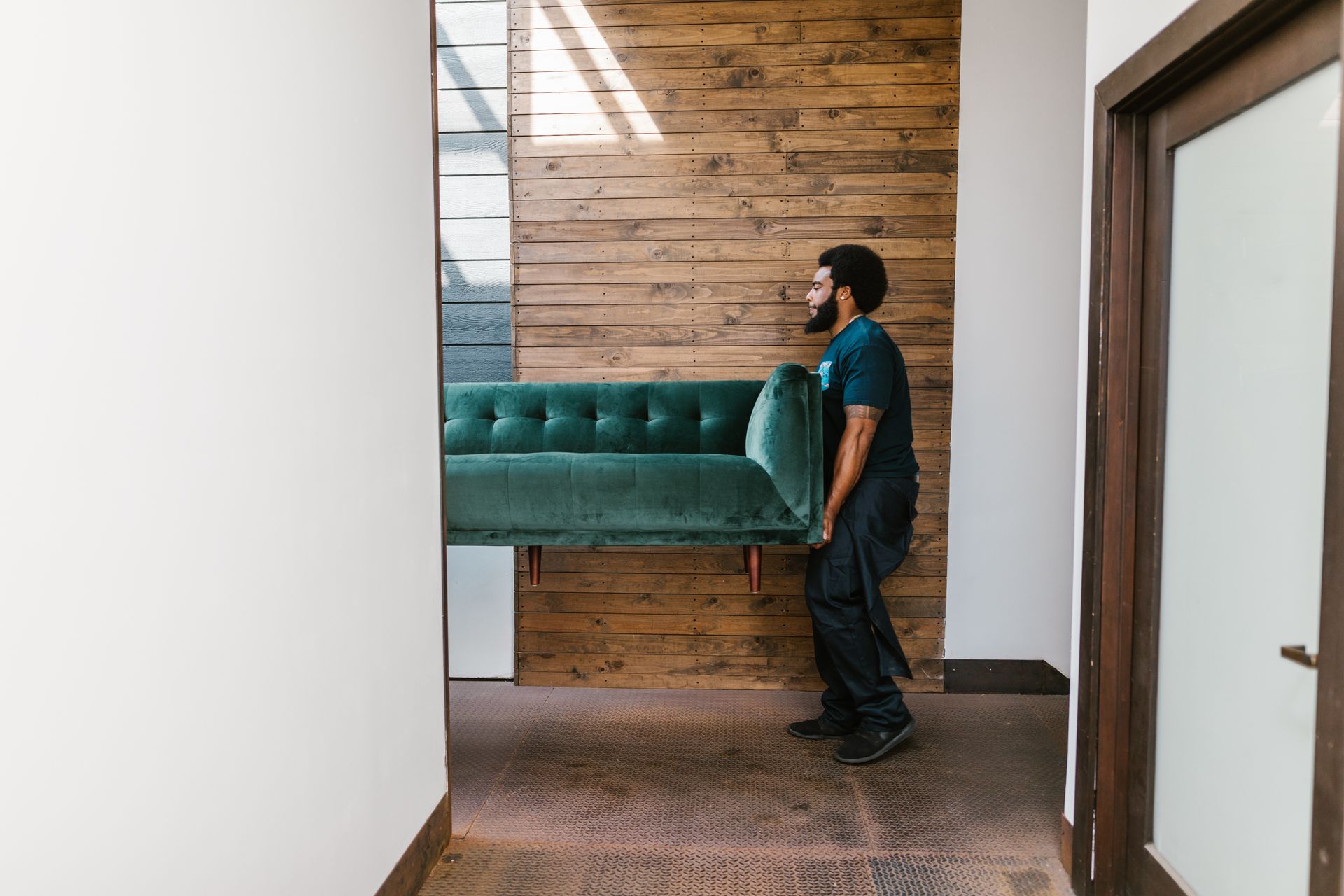 A mover in a dark uniform carrying a green velvet sofa through a residential doorway